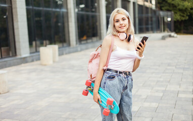 Wall Mural - Cool young girl with skateboard using smartphone in the city