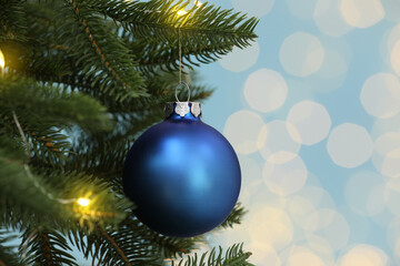 Beautiful blue bauble hanging on Christmas tree against blurred festive lights, closeup