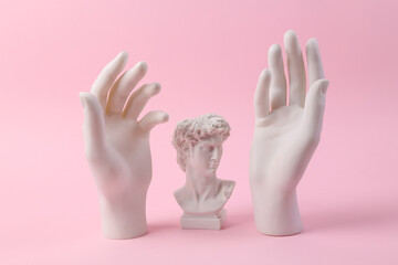 Wall Mural - Antique bust of David with statues of hands on a pink background. Minimal still life