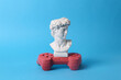 Antique David bust with gamepad on blue background. Gaming. Conceptual pop. Minimal still life.