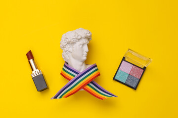 Wall Mural - David Bust in rainbow tape with lipstick and eye shadow palette on yellow background. Minimal beauty still life. Flat lay