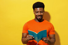 Young Smiling Student Man Of African American Ethnicity 20s Wear Orange T-shirt Read Novel Book Learn Prepare Before Exam Isolated On Plain Yellow Background Studio Portrait. People Lifestyle Concept.