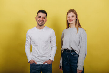 Two young beautiful people girl and guy standing on a yellow background.