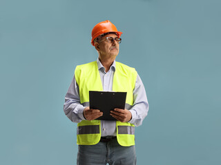 Mature male engineer with a clipboard and safety vest looking to the side