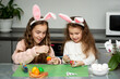 © Natalya Temnaya - Two girls in hare ears paint eggs. Easter. They are at home in the kitchen. Preparation for the holiday.
