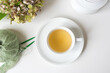 High angle closeup of herbal tea in white cup and saucer on table with knitting and dried hydrangeas (selective focus)
