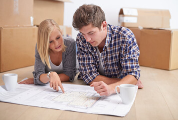 Wall Mural - Deciding where to put all their furniture. A young couple lying on the floor with the blueprints of their new flat and boxes behind them.