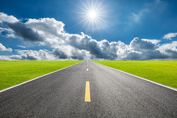 Straight asphalt highway and green grass under blue sky