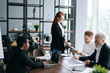 © dikushin - Confident female team leader wearing glasses holding corporate meeting with multi-ethnic colleagues in office. Serious businesswoman discussing project with business partners at table in boardroom.