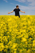 © Margarita Timofeeva - Man in black t-shirt is enjoying nature in the middle of field full of yellow flowers. Yellow field of flowering rapeseed with cloudy blue sky - brassica napus - plant for green energy, medicine.