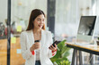 © PaeGAG - Asian business woman in cafe using mobile phone. Girl chatting on smartphone and drinking coffee in restaurant near window, smiling at cellphone screen.