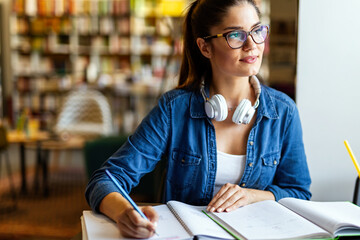 Wall Mural - Portrait of happy young female studying in a library. Education study teenager concept