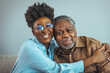 Close up faces of elderly 80s grandfather adult 30s granddaughter. Teenager girl sitting on window with father. Beautiful African American woman with her father as they both smile