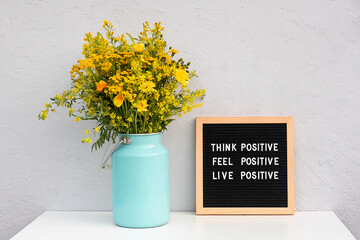 Wall Mural - Think positive, feel positive, live positive. Motivational quote on letter board and bouquet yellow flowers on white table against grey stone wall. Concept inspirational quote of the day