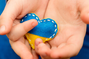 Ukraine flag theme. Heart shape pin badge made of blue and yellow stuffed felt in child hand. Topical issues of war. Freedom fighters. Support of nations, unity