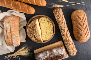 Wall Mural - bread background. various kinds of fresh delicious bread on wooden boards and a cloth towel. top view. black table.