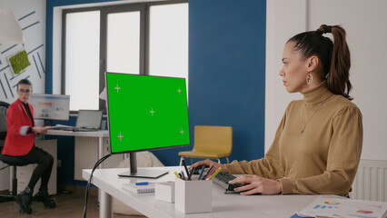 Business woman looking at green screen on computer, using isolated template and chroma key mock up template on monitor display. Employee working with blank copy space background.