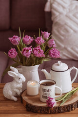 Wall Mural - Still-life. A vase with flowers, tulips, a teapot, a bunny, a candle and a cup of tea on the coffee table in the living room home interior. Cozy spring concept.