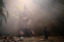 Man In Jungle Morning Performing A Religious Ritual Infront Of Small Statue Of Terracotta Warrior, Holding Hands Above Head While Praying. 