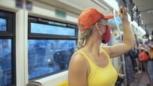 Woman Travel Caucasian Ride At Overground Train Airtrain With Wearing Protective Medical Red Mask. Girl Tourist At Airtrain With Respirator. Pandemic Virus Coronavirus Covid-19. People In Mask.