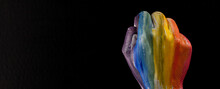 A Hand Clenched Into A Fist Painted In Rainbow Colors. Black Color In The Background.