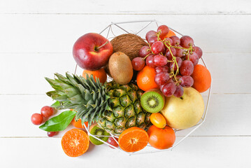 Basket with juicy fruits on white wooden background