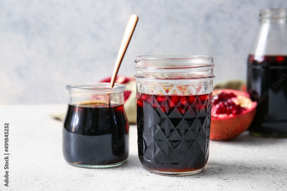 Jars of pomegranate molasses on light background