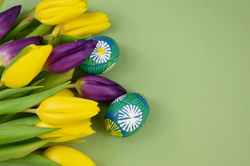 Wall Mural - Beautiful hand painted easter eggs with yellow and purple tulips frame stock images. Easter colored eggs isolated on a green background with copy space for text stock photo. Spring easter eggs border