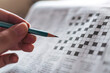© artitwpd - Close up hand holding pencil over crossword puzzle on newspaper. Game on for writing some letters to solve and completing the empty table. Focus on empty crossword table.