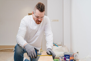 carpenter in protective gloves and glasses makes measurements on wood