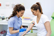 © Graphicroyalty - Preparation for blood test with pretty young woman by female doctor medical uniform on the table in white bright room. Nurse pierces the patient's arm vein with needle blank tube.