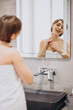© Petro - Young woman looking into the mirror and using jade face roller at home