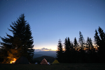 brightly illuminated camping tents glowing on campsite in dark mountains under night stars covered s