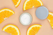 Moisturizing cream with orange extract. Open jar of cream and orange slices on beige background