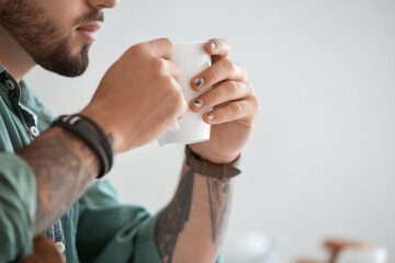 Wall Mural - Man with stylish manicure holding cup on light background, closeup