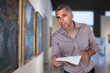 © JackF - Adult man is visiting museum with information brochure and looking at the pictures in the gallery indoor.