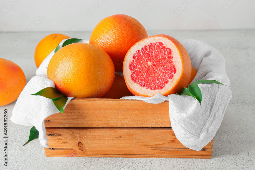 Box with delicious grapefruits on light background