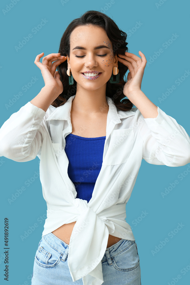 Attractive young woman with glitters on her face against blue background