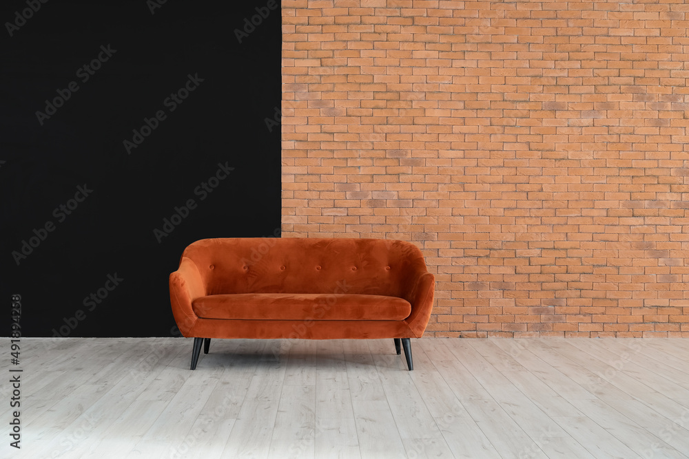 Red sofa near black and brick wall in big empty room