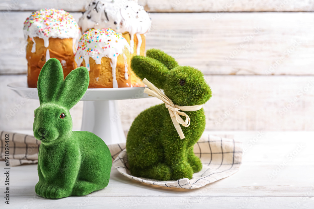 Cute Easter bunnies and stand with cakes on light background
