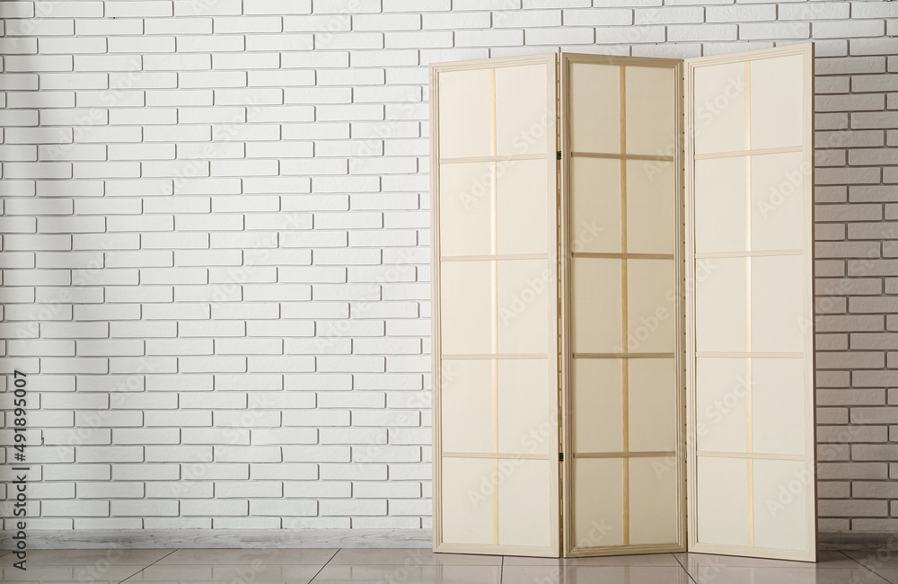 Stylish folding screen near light brick wall in room