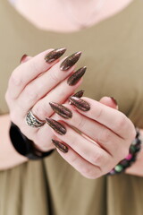 Female hand with long nails and a bottle of brown green nail polish