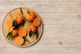 Fototapeta Kuchnia - Fresh cutted clementines and whole mandarin over round plate on colored background. Food and drink ingredients preparing. healthy eating theme top view vith copy space
