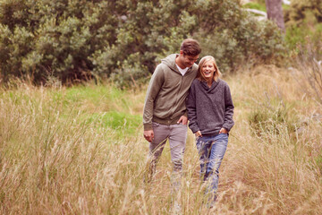 Wall Mural - Marriage can be a walk in the park. A young couple laughing as the walk in a field.