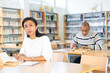 © JackF - Portrait of focused adult Latina studying in university library, making notes in workbook