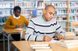 © JackF - Young adult man working with books, finding information at library