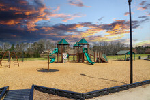 Children Playing On A Green And Brown Jungle Gym At The Park With A Green Slide Surrounded By Bare Winter Trees And Lush Green Trees With Red Sky And Clouds At Swift Cantrell Park In Kennesaw Georgia