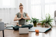 © Sviatlana - Athletic woman doing yoga and watching online lessons on laptop, exercising in living room