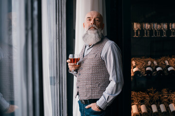 Wall Mural - handsome man with a glass of wine standing near a rack of wine samples.