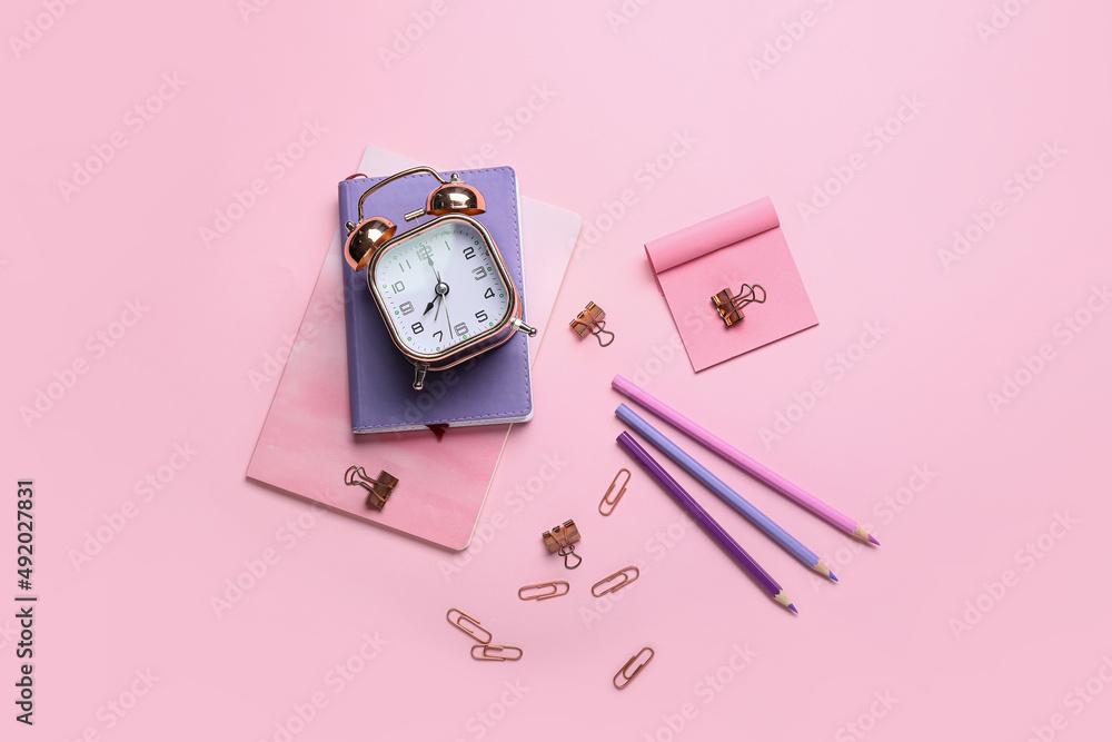 Set of stationery and alarm clock on pink background